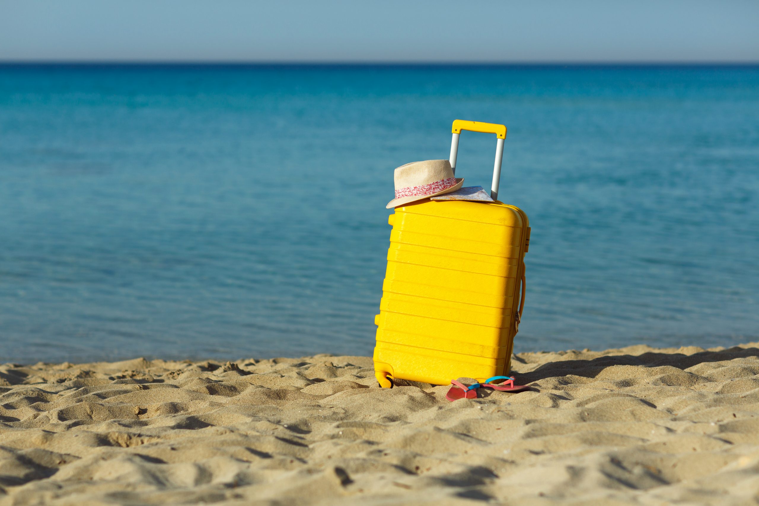 Travel holiday vacation yellow suitcase with map, straw hat and beach slippers on the beautiful sand beach on SelfishMe Travel